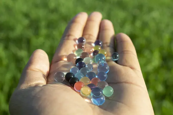 Colorful glass balls in hand on the green grass background, close up