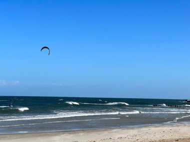 Dalgalar denizin güneşli bir gününde geniş bir kumsala çarpıyor.