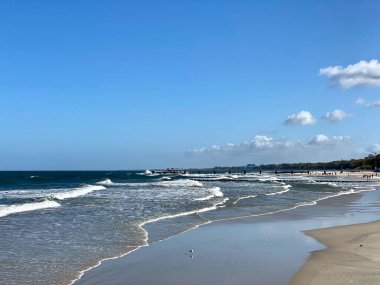Dalgalar denizin güneşli bir gününde geniş bir kumsala çarpıyor.
