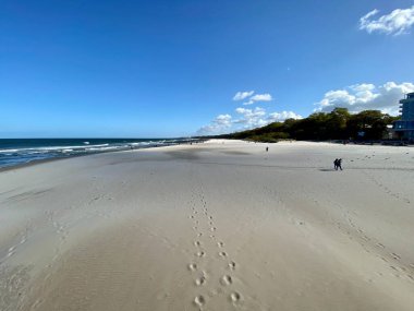 Dalgalar denizin güneşli bir gününde geniş bir kumsala çarpıyor.