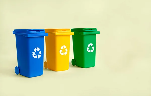 Blue, yellow and green container for separate plastic, paper and organics garbage collection, isolated on the yellow background with copy space, waste recycling concept