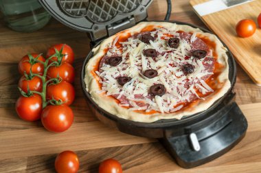 Homemade pizza waffle with pepperoni, olives and parmesan cheese ready to bake in a waffle iron clipart