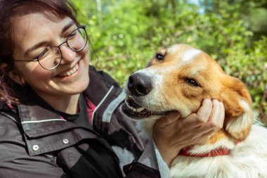 Evcil köpeği açık havada gülümseyen genç bir kadın.