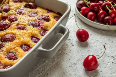 Clafoutis vişneli turta - geleneksel Fransız turtası ve gri masada taze kirazlar.