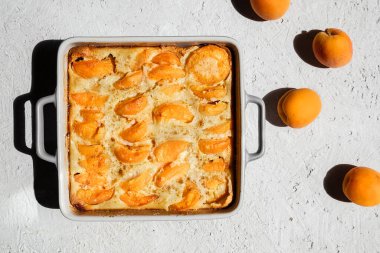 Kayısılı Clafoutis. Fırın kabında yaz turtası ve ışık masasında taze kayısılar.