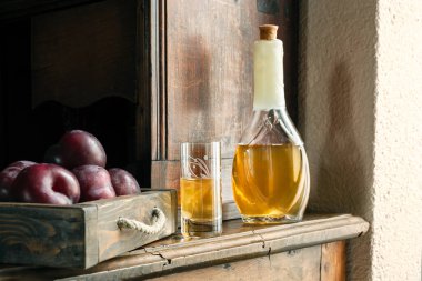 Geleneksel Balkan erik brendisi - rakia slivovica veya rakija şişede, sljivovica 'lı bir şarap bardağı ve eski büfede gün ışığında taze erikler.