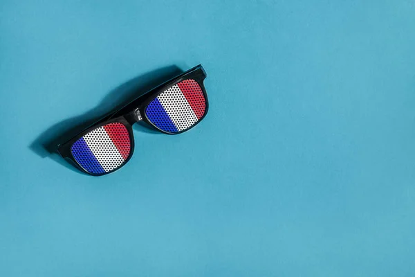 Sunglasses in the colors of the French flag on blue background top view, French National Day