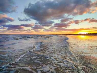 Altın gün batımı okyanus dalgalarını yansıtır. Renkli bulutlarla sakin bir atmosfer yaratır..