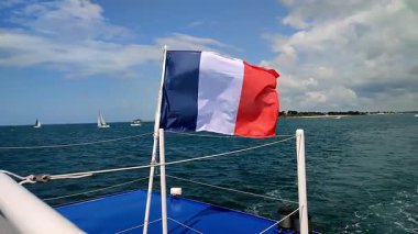 Mavi okyanus ve uzak yelkenli teknelerle çevrili Fransız bayrağı dalgalanır, canlı bir deniz keşfi ve macera ortamı yaratır.