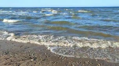 Sakin dalgalar yavaşça kumlu sahile vuruyor, güneş ışığını yansıtıyor ve huzurlu bir atmosfer yaratıyor, rahatlamak ve doğayı takdir etmek için mükemmel.