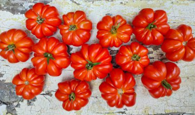 Canlı kırmızı aile yadigarı domatesler kırsal ahşap bir yüzey üzerinde sanatsal olarak düzenlenir. Mutfak yaratıcılığı için eşsiz şekillerini ve dokularını vurgularlar.