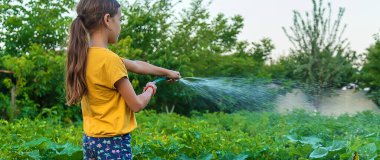 The child is watering the garden with a hose. Selective focus. Nature.