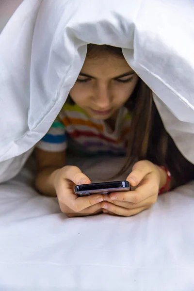 The child plays with the phone in bed. Selective focus. Kid.