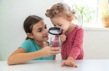 Çocuk bir büyüteç altında suyu inceler. Seçici odaklanma. Çocuk.