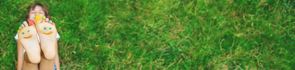 緑の芝生の上で笑顔の塗料のパターンを持つ子供の足 選択的フォーカス — ストック写真