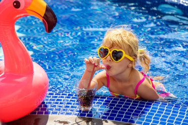 Güneş gözlüklü bir çocuk havuz kenarında kokteyl içer. Seçici odaklanma. Çocuk.