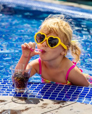 Güneş gözlüklü bir çocuk havuz kenarında kokteyl içer. Seçici odaklanma. Çocuk.