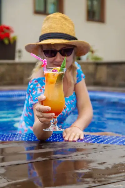A woman in the pool drinks a cocktail. Selective focus. Kid.