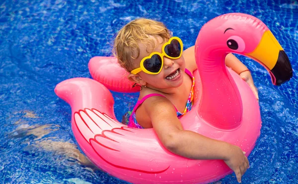 A child in a pool swims in a circle of flamingos. Selective focus. Kid.