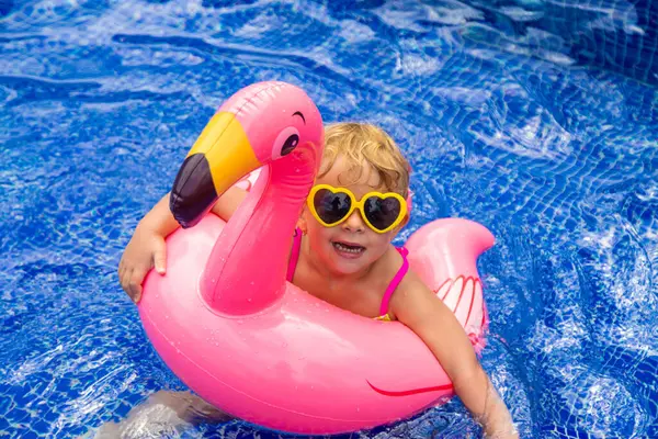 A child in a pool swims in a circle of flamingos. Selective focus. Kid.