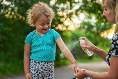 Annem çocuğuna sivrisinek kovucu sıkar. Seçici odaklanma. Doğa.