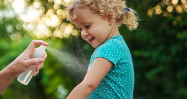 Annem çocuğuna sivrisinek kovucu sıkar. Seçici odaklanma. Doğa.