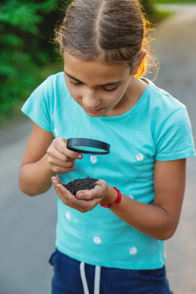 Çocuk bir büyüteçle ellerindeki toprağa bakıyor. Seçici odaklanma. Çocuk,