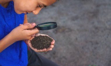 Bir çocuk büyüteçle toprağa bakar. Seçici odaklanma. Çocuk.
