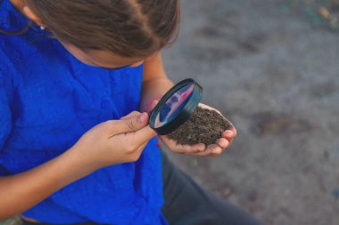 Bir çocuk büyüteçle toprağa bakar. Seçici odaklanma. Çocuk.