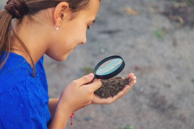 Bir çocuk büyüteçle toprağa bakar. Seçici odaklanma. Çocuk.