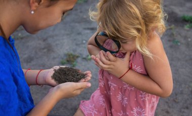 Bir çocuk büyüteçle toprağa bakar. Seçici odaklanma. Çocuk.