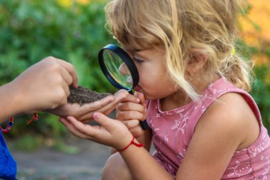 Bir çocuk büyüteçle toprağa bakar. Seçici odaklanma. Çocuk.