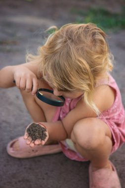 Bir çocuk büyüteçle toprağa bakar. Seçici odaklanma. Çocuk.