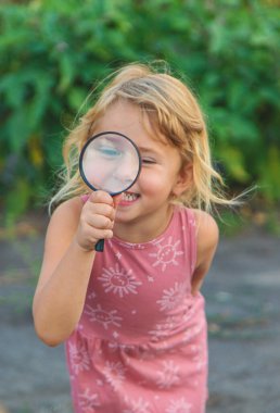 Bir çocuk doğadaki büyüteçten bakar. Seçici odaklanma. Çocuk.