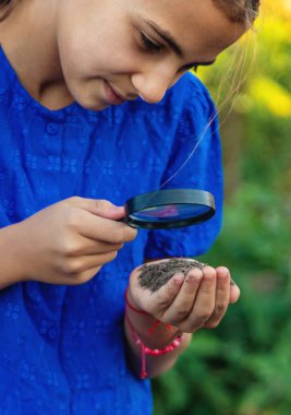Bir çocuk büyüteçle toprağa bakar. Seçici odaklanma. Çocuk.