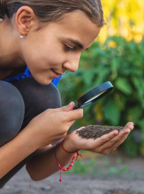 Bir çocuk büyüteçle toprağa bakar. Seçici odaklanma. Çocuk.