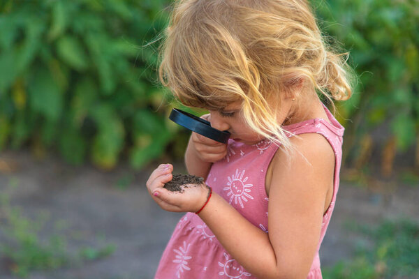 Ребенок смотрит на почву через лупу. Выборочный фокус. Kid.