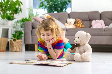 Evde oyuncak ayıyla kitap okuyan bir çocuk var. Seçici odaklanma. çocuk.