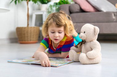 Evde oyuncak ayıyla kitap okuyan bir çocuk var. Seçici odaklanma. çocuk.