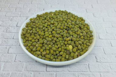Pile of mung beans or Vigna Radiata in a white plate. This food source containing high levels of vegetable protein is rich in fiber and prebiotics. clipart