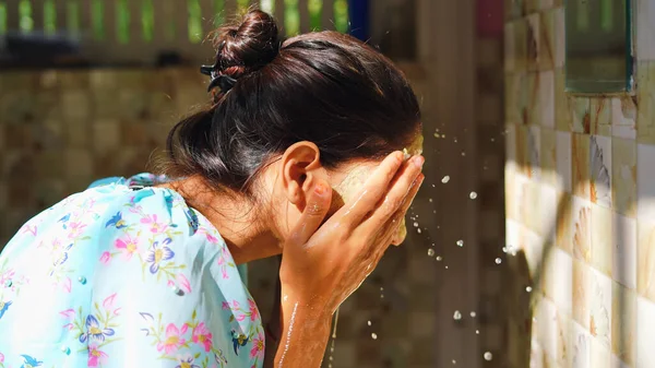 Beautiful woman is washing facial mask in bathroom after applying face mask. Girl spraying water on her face standing in front of mirror at home. mud mask or homemade multani mitti mask.