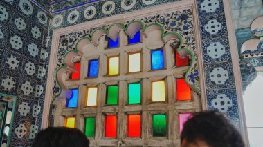 Udaipur, Rajasthan, Hindistan 'daki Şehir Sarayı renkli pencere manzarası. Müzedeki mozaik pencerelerden kasaba manzarasına bakan insanlar. İçerisi, iç görünüş