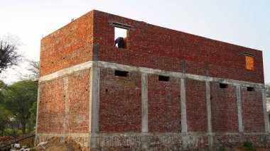 İnşaat altındaki tuğla bir binanın penceresinde duran bir zanaatkar yapıyı şekillendirmeye çalışıyor. İş yerinin dış duvarında betonla kaplanmış biri var. İnşaatçı, mühendis, işçi