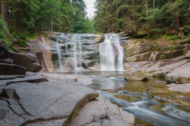 Mumlava şelalesi, sağ ön planda, nehir kenarında. Dağ Nehri Mumlava, Krkonose Ulusal Parkı, Çek Cumhuriyeti, yaz öğleden sonra.