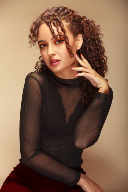 Yüzü yüzüne yakın oturan, kırmızı makyaj yapan ve bej arka planı olan bir kadının etkileyici portresi.