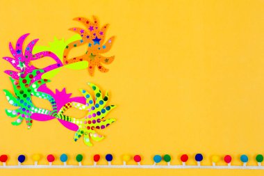 Bir çift canlı kağıt maske, güneşli sarı bir zemin karşısında tek başına duruyor, neşeli ve şenlikli bir sahne yaratıyor.