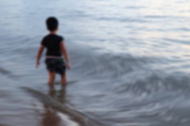 Blured photo of a rear view of a boy stand on the shore of the beach looking at the water. and he is going play water which it dangerous swimming alone