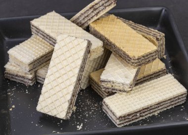 Çatlak çikolata dolu gofretler, gofret dilimleri, siyah tabakta uzun kesilmiş bisküvi çubukları..