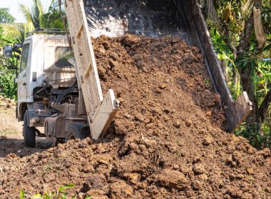 Beyaz renkli bir çöp kamyonu göleti doldurmak için toprak döküyor..