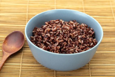 Sağlıklı pişirilmiş kahverengi pirinç, yanında tahta kaşıkla gri bir seramik kasede riceberry ile karıştırılmış..